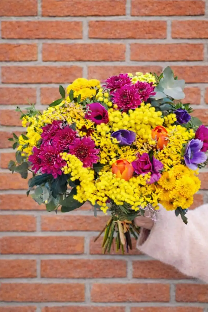 Mazzo di mimosa, rose fucsia e fiori viola davanti a un muro di mattoni