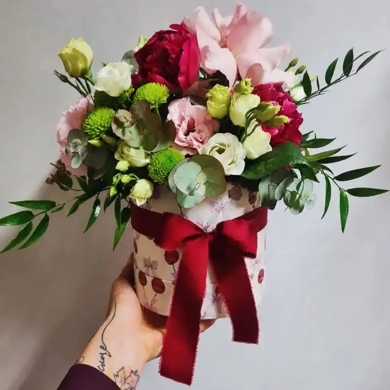 Cappelliera con rose, lisianthus e fiocco rosso tenuta in mano
