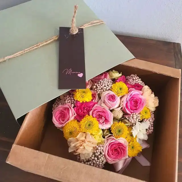 Scatola di cartone piena di rose rosa e fiori gialli