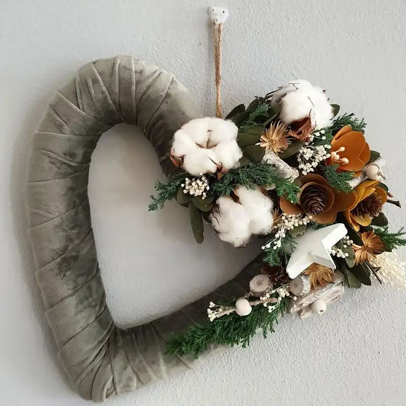Cuore di velluto verde con cotone, pigne e fiori secchi appeso al muro